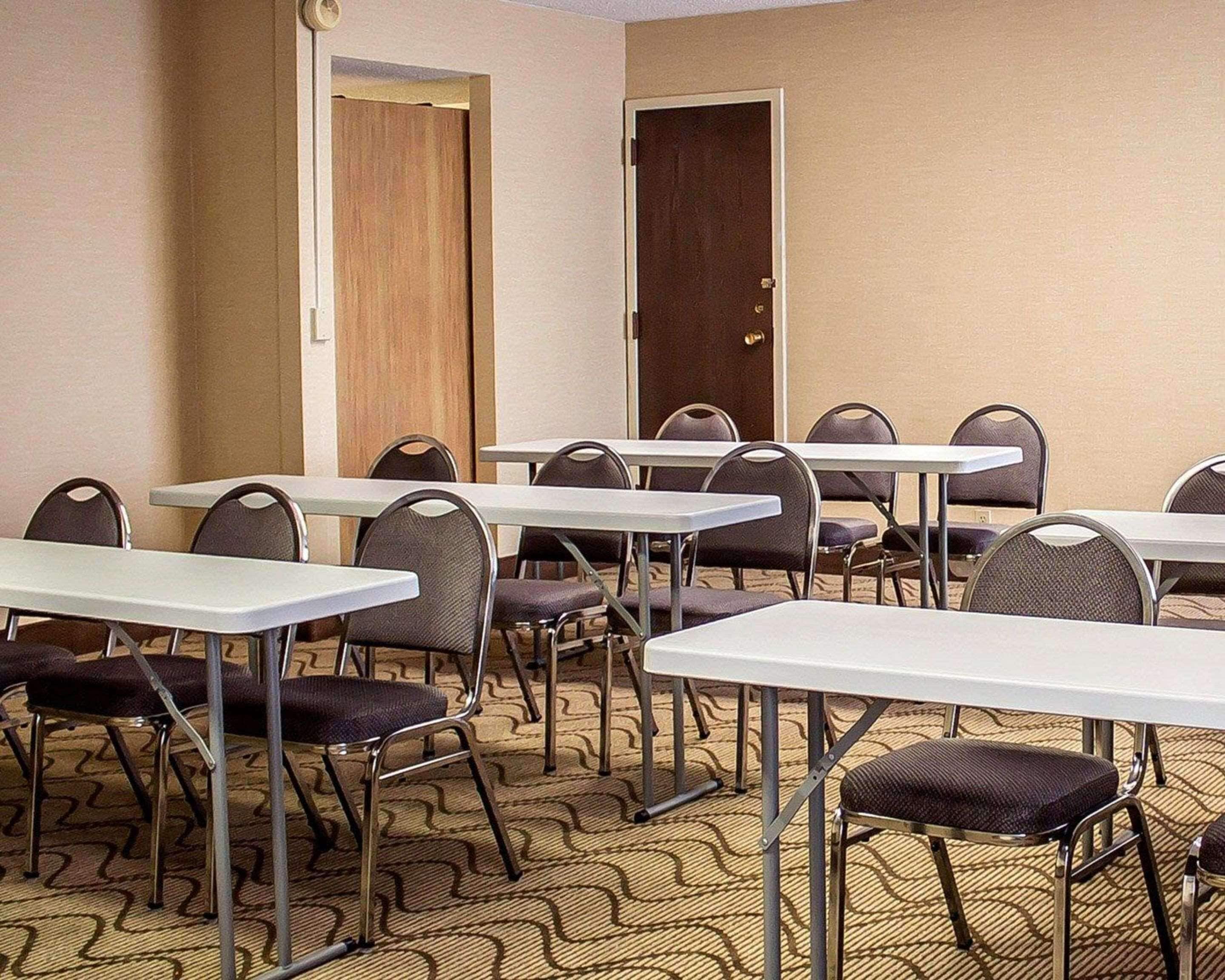 Sala de conferências com mesas, cadeiras, piso coberto por carpete e portas.