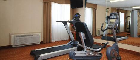 Une chambre d’hôtel équipée d’un tapis de course, d’un vélo d’appartement, d’un téléviseur fixé au mur et d’une horloge.