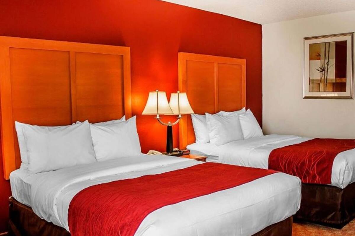 Una habitación de hotel con dos camas, una pared roja y un cuadro colgado.