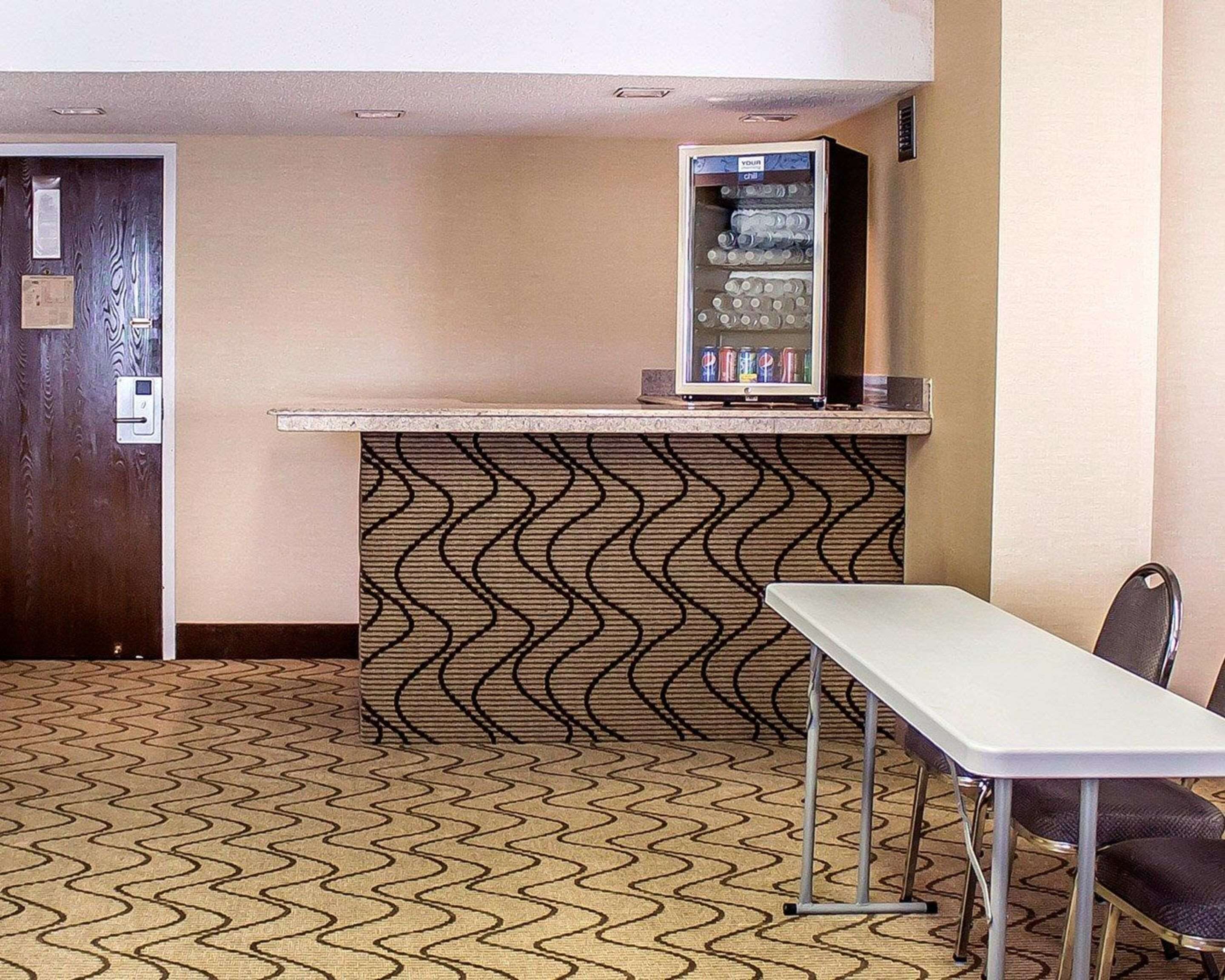 A small kitchenette with a refrigerator, a microwave, and a sink. There is a table and a chair in front of the kitchenette.