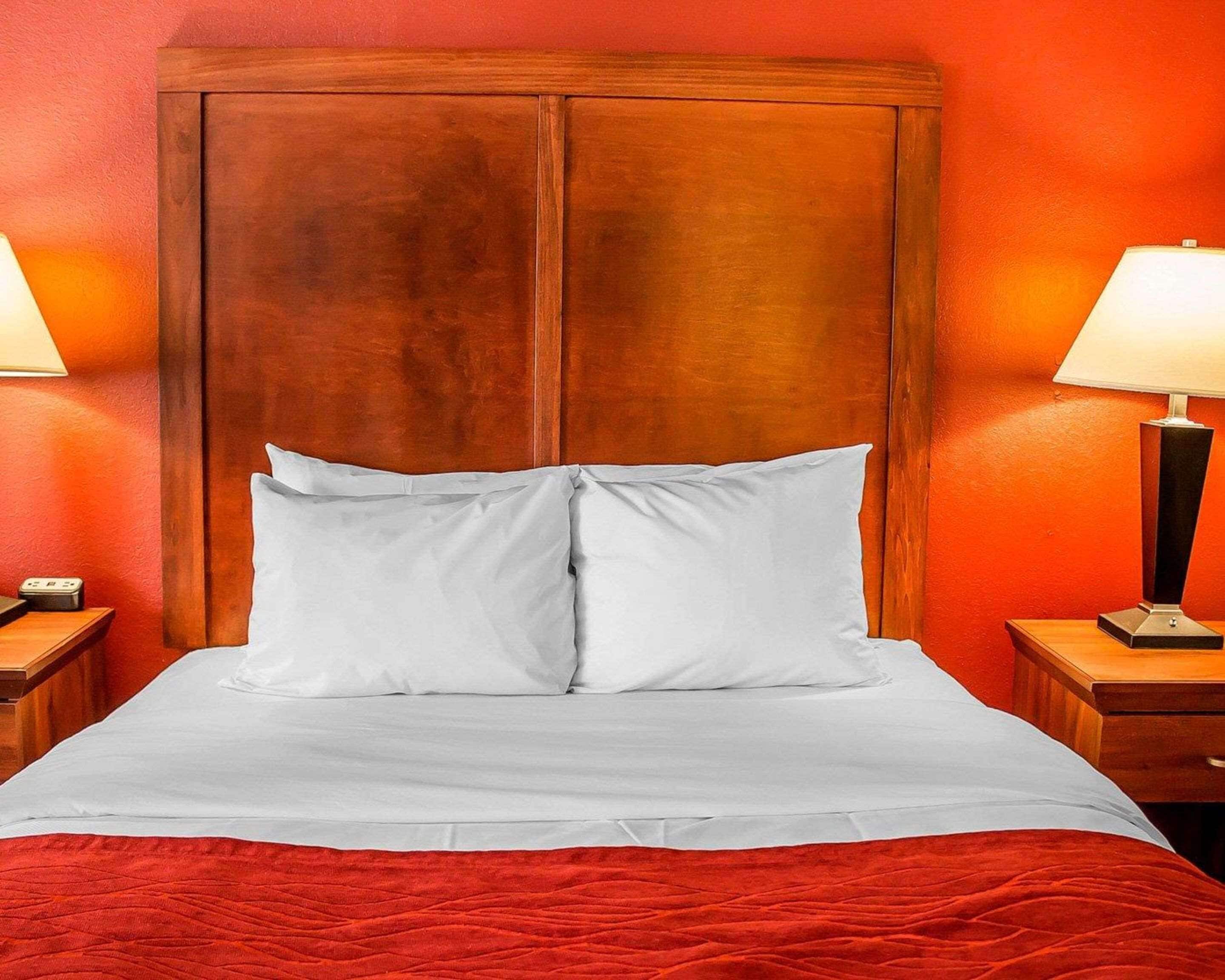 A hotel room with a wooden headboard, white bedding, and red walls.