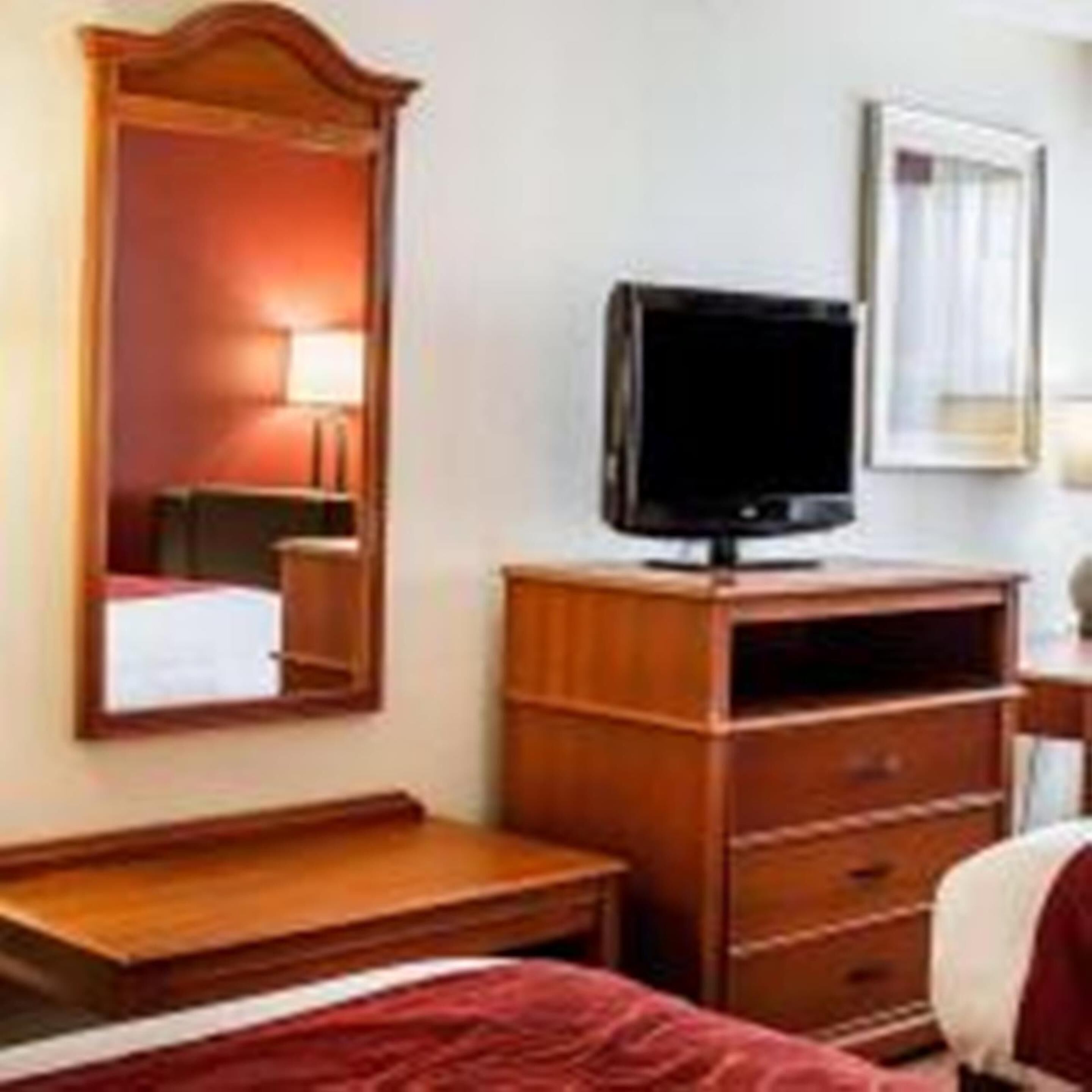 A hotel room with a bed, a wooden dresser, a television on top of the dresser, and a mirror on the wall.