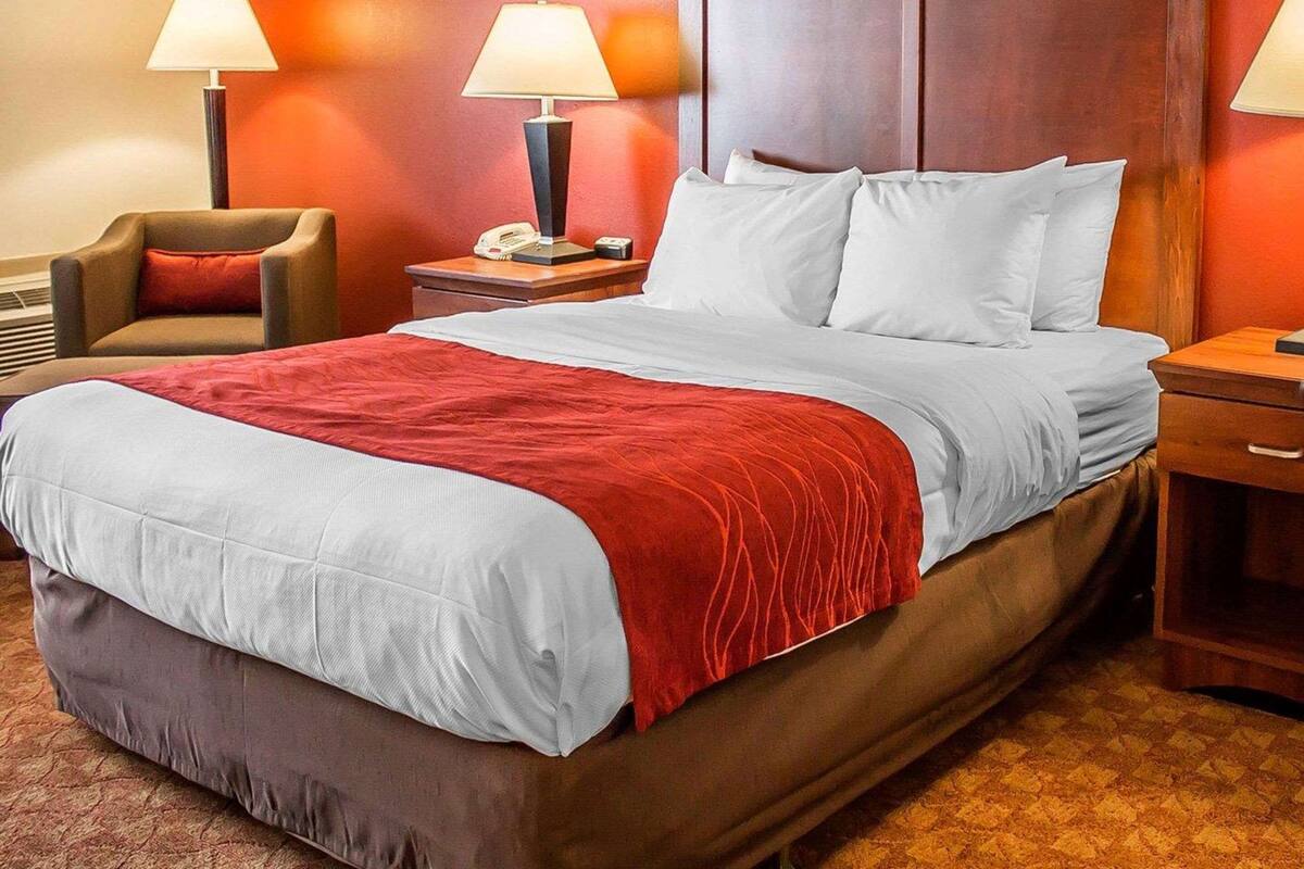 Habitación de hotel con una cama grande, dos lámparas de noche, una silla y una mesita de noche con un teléfono y un reloj.