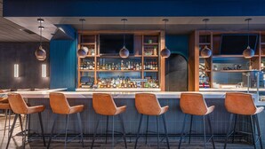 A bar area with a long counter, multiple stools, and a well-stocked shelf with various bottles.