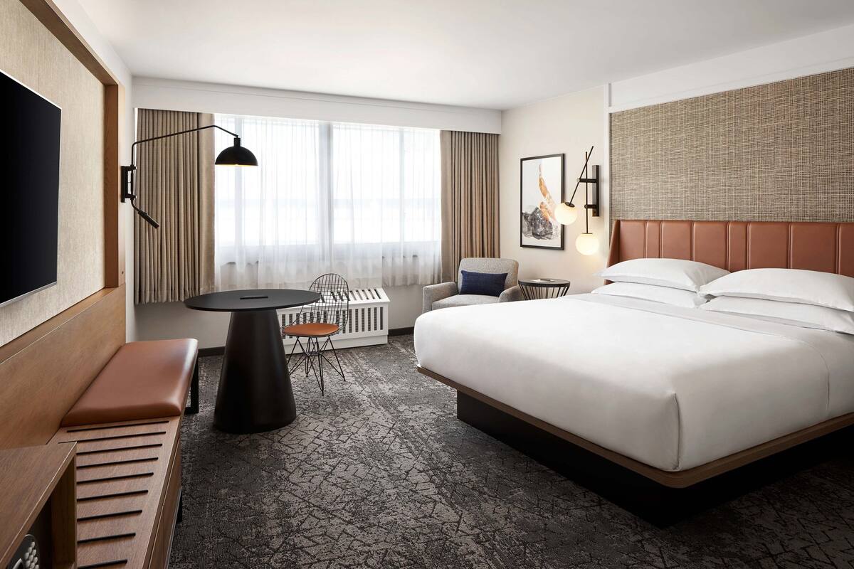 A hotel room with a large bed, a desk with a chair, a television, and a window with curtains.