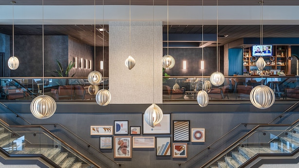 A modern lobby with a staircase, hanging pendant lights, and framed artwork on the walls.
