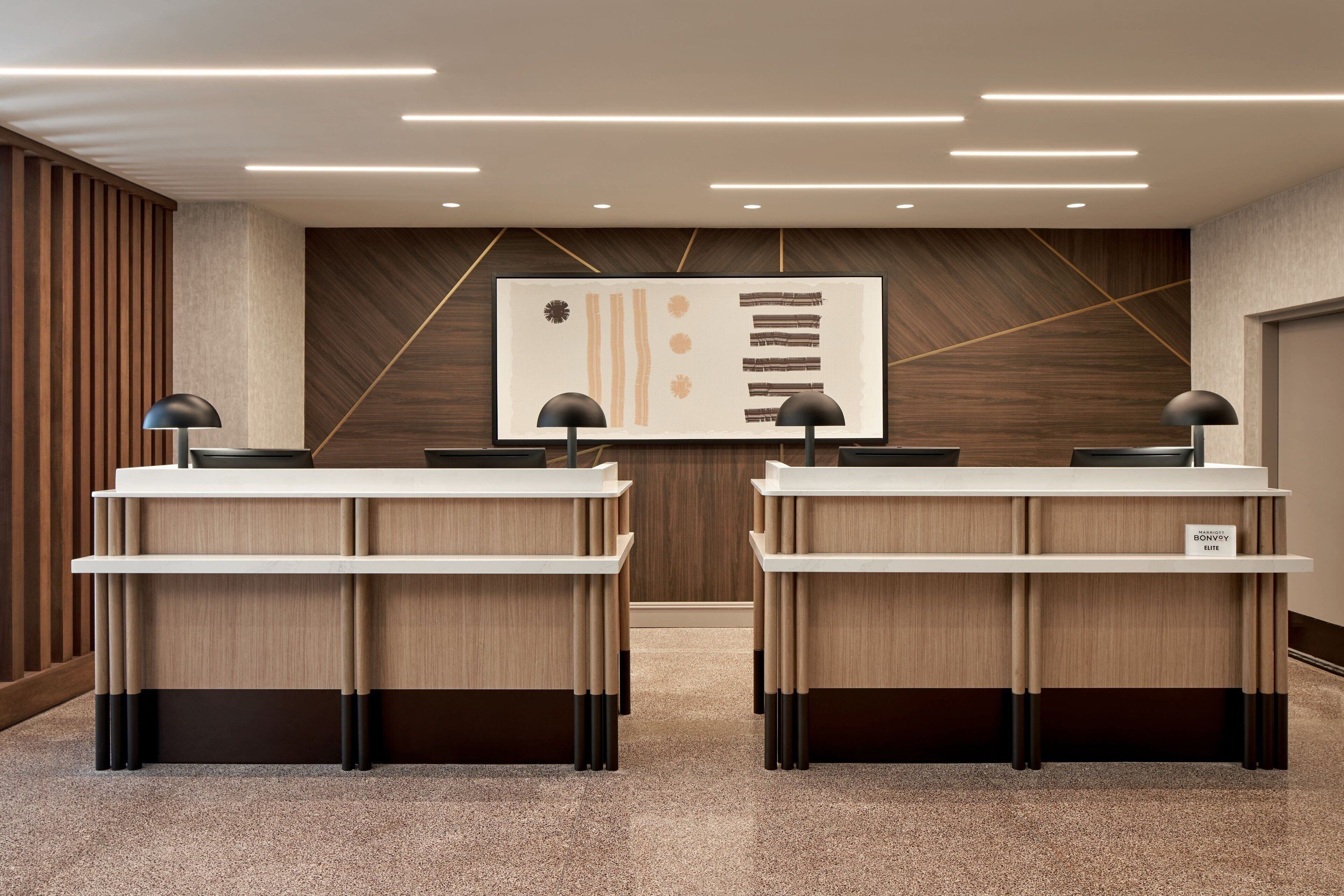 A reception area with two desks, a modern wall art piece, and a wooden panel design on the wall.