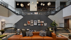 A spacious lobby with a modern brown leather sofa, a staircase, and a wall adorned with framed artwork.