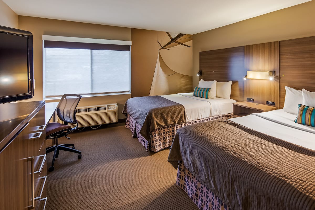 Habitación de hotel con dos camas, un escritorio con silla, televisión y un ventanal grande.
