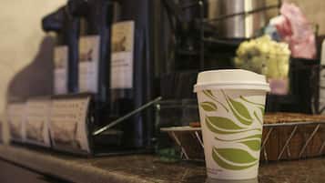 A coffee cup with a leaf design on a countertop, a coffee machine, and a muffin tray in the background.