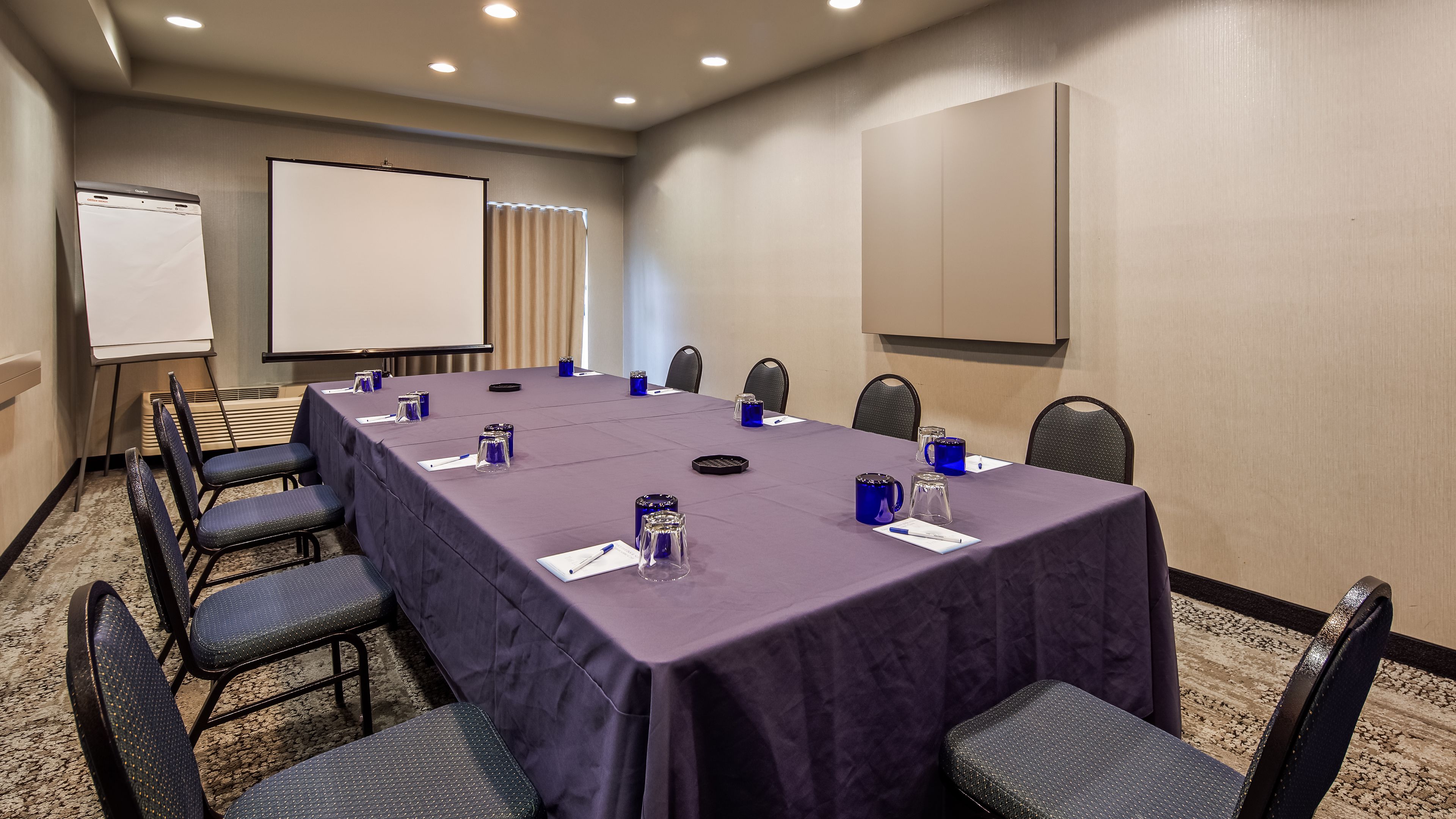 Una sala de conferencias con una larga mesa, sillas, una pizarra y una pantalla para proyector.