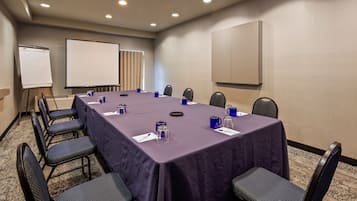 A conference room with a long table, chairs, a whiteboard, and a projector screen.
