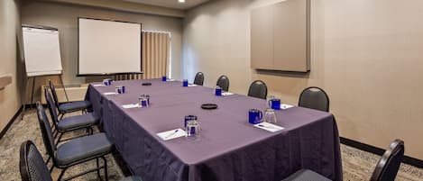 Una sala de conferencias con una larga mesa, sillas, una pizarra y una pantalla para proyector.