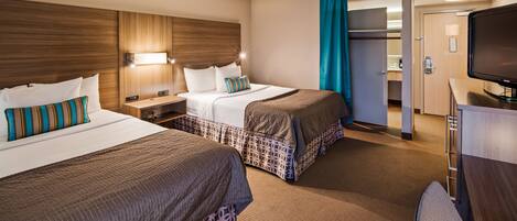 A hotel room with two beds, a TV, a desk, and a bathroom visible through an open door.