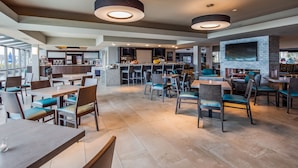 A modern restaurant with high tables and chairs, a bar area, and a fireplace. - Executive Inn & Suites Embarcadero Cove (Oakland)