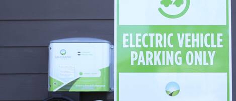A sign indicating electric vehicle parking only, with a charging station and a warning that other vehicles may be towed at the owner's expense.