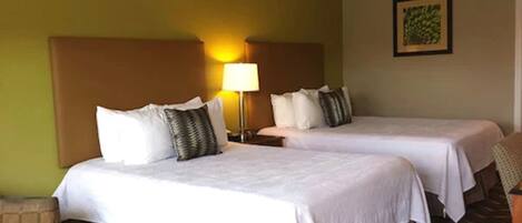 A hotel room with two beds, a nightstand with a lamp, and a framed picture on the wall.
