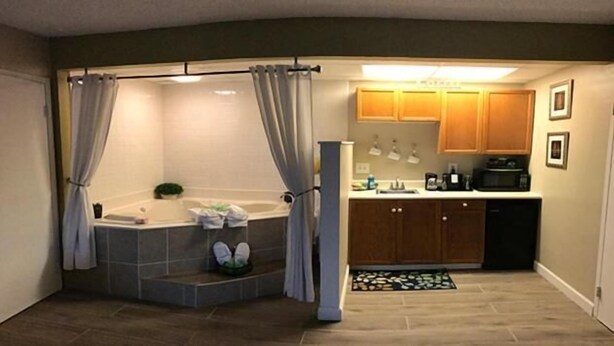 A bathroom with a bathtub, shower, and toilet. There is a small sink and a toilet paper holder. The bathroom has a shower curtain and a towel rack. - Wingfield Inn (Mayfield)