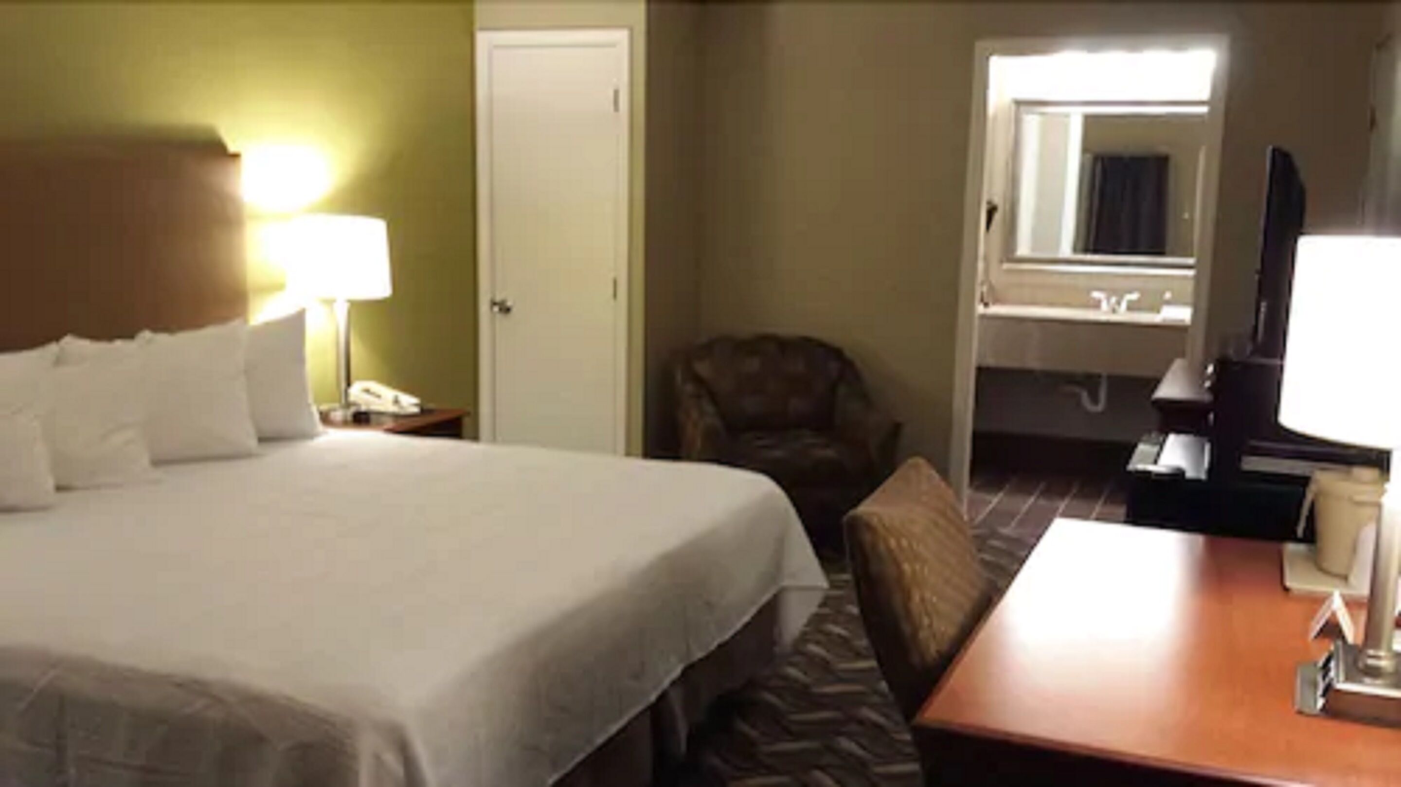 Una habitación de hotel con una cama grande, una silla, un escritorio con lámpara y una ventana.