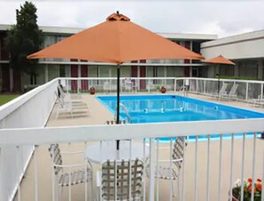 A swimming pool with a white deck and a metal railing. There are lounge chairs and an orange umbrella.