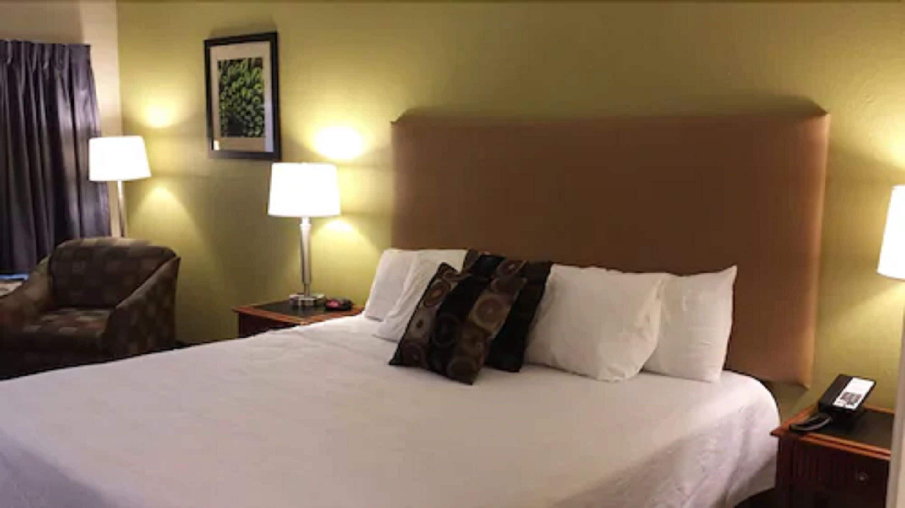 A hotel room with a large bed, two bedside lamps, a chair, and a framed picture on the wall.
