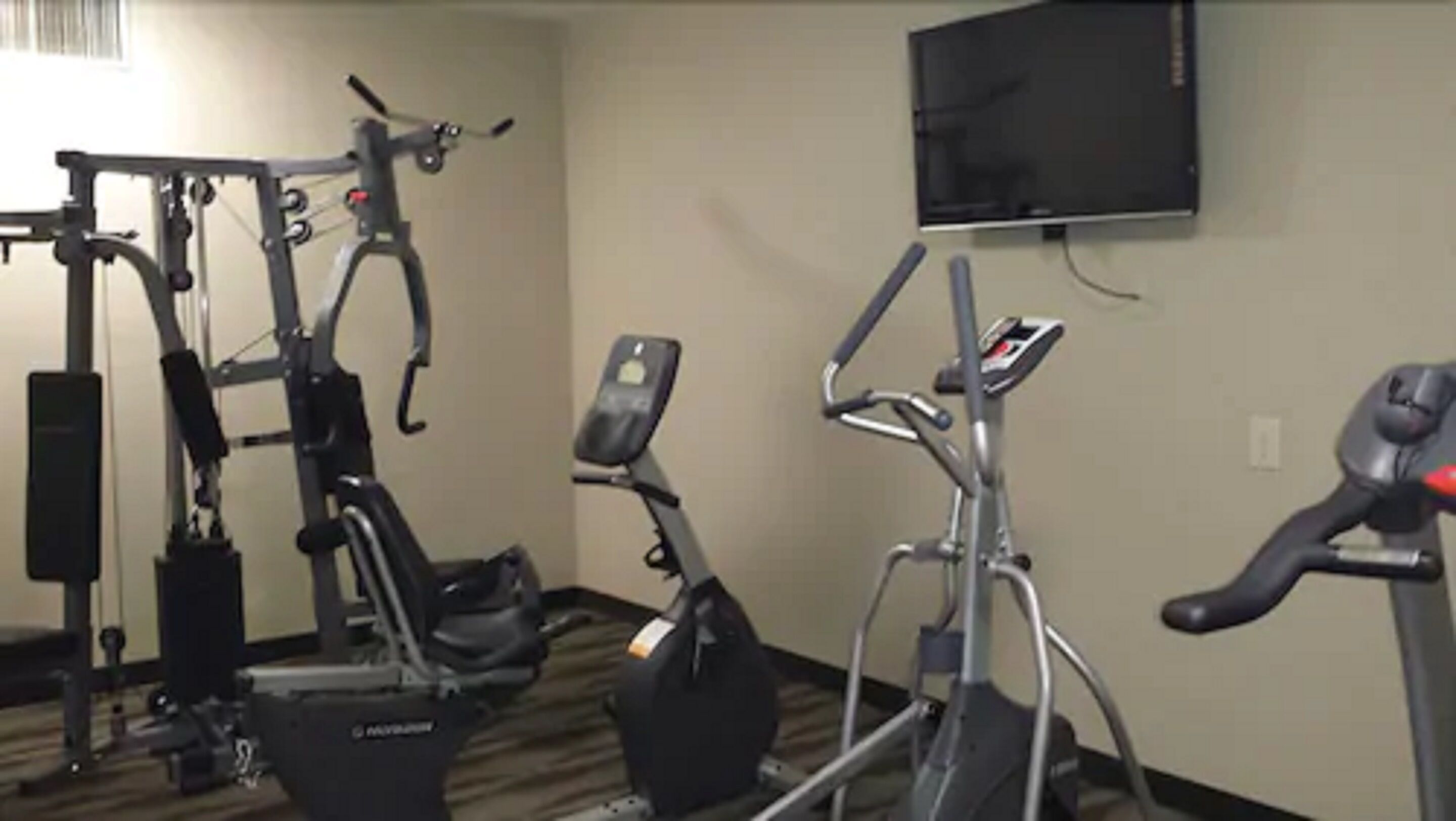 Un gimnasio con diferentes equipos de ejercicio, incluyendo una bicicleta estática, una máquina elíptica y un aparato de pesas.