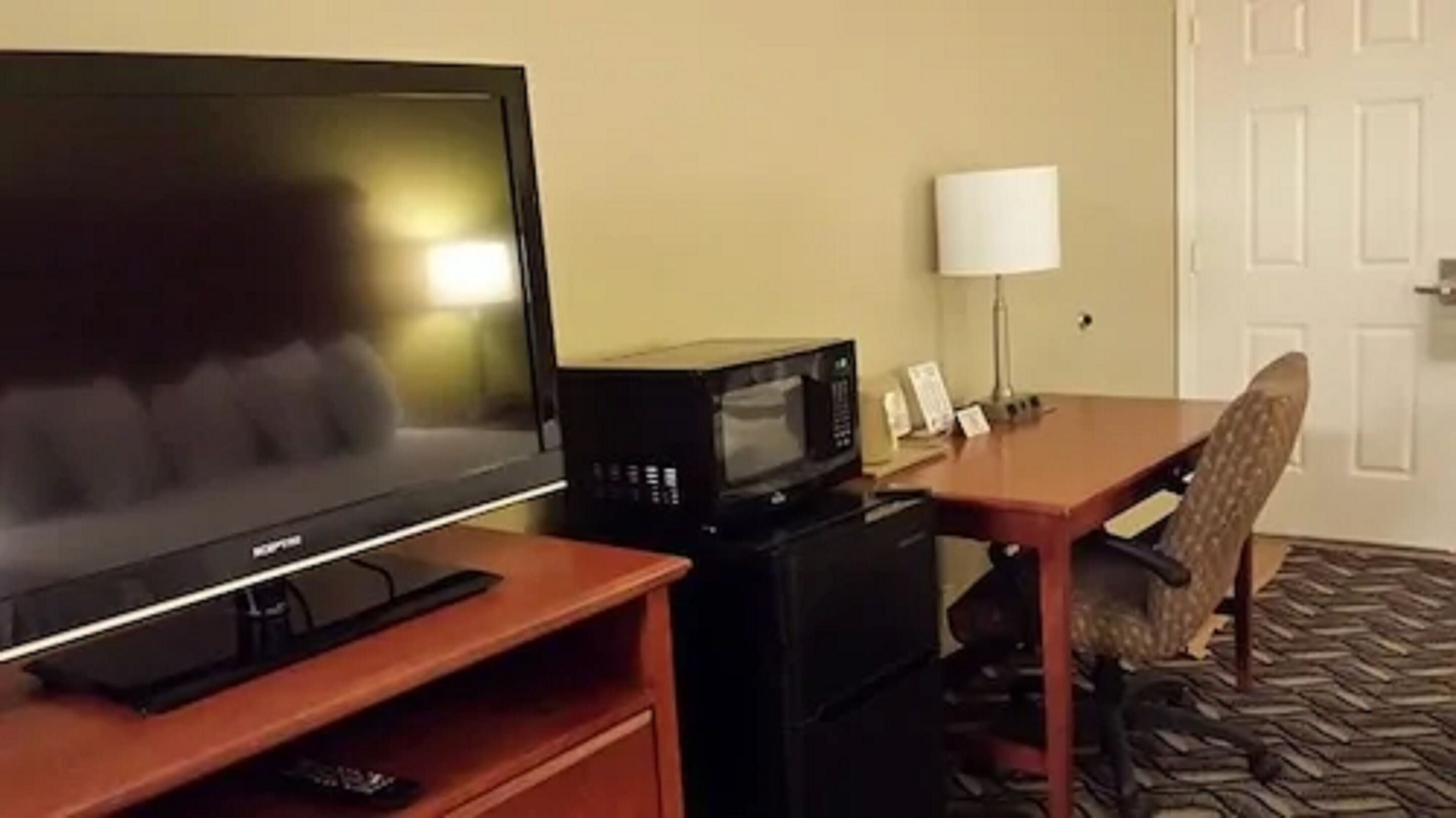 A hotel room with a television, a microwave, a lamp, and a chair.