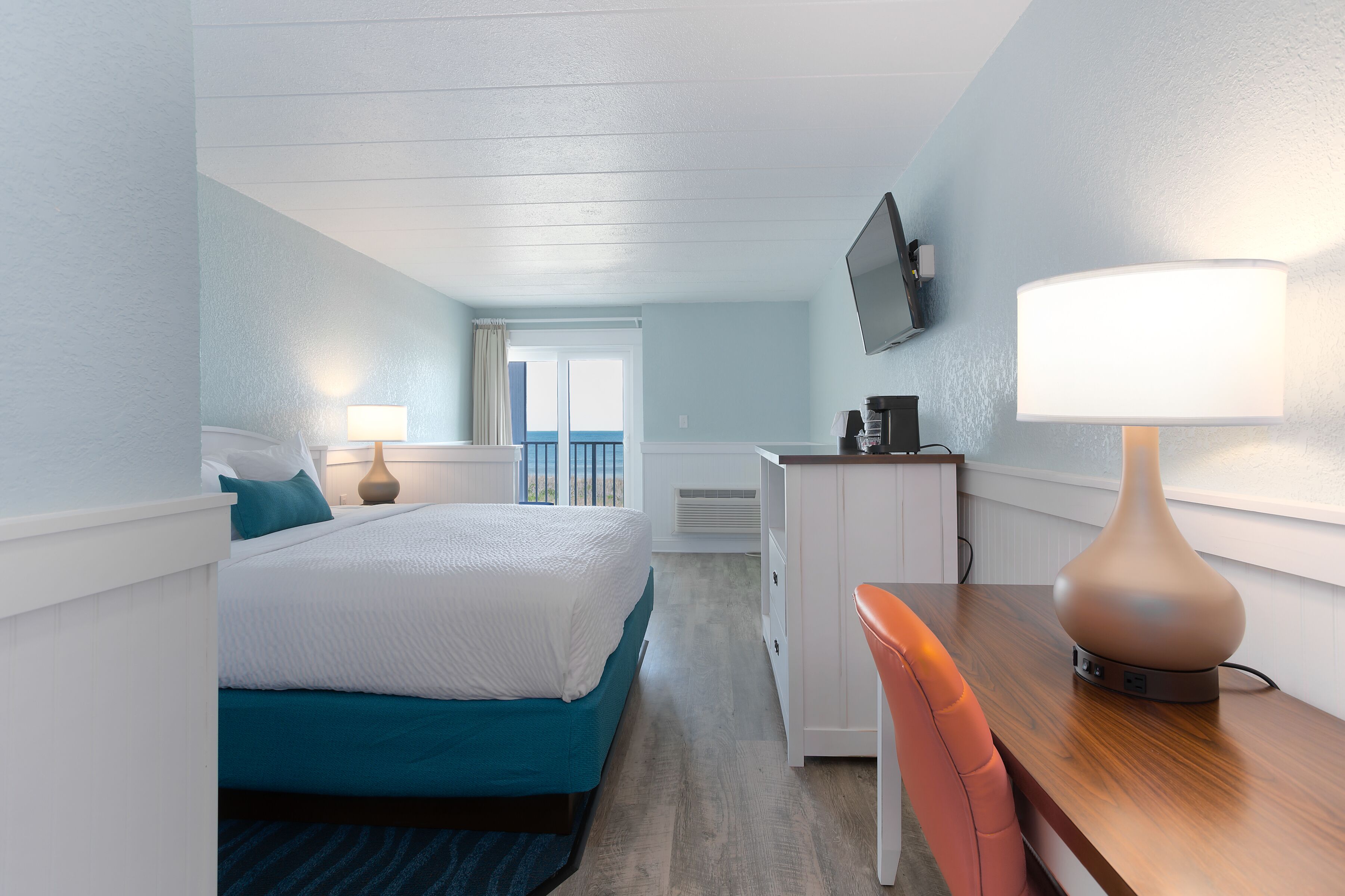 A hotel room with a bed, a desk, a chair, a TV, and a lamp.
