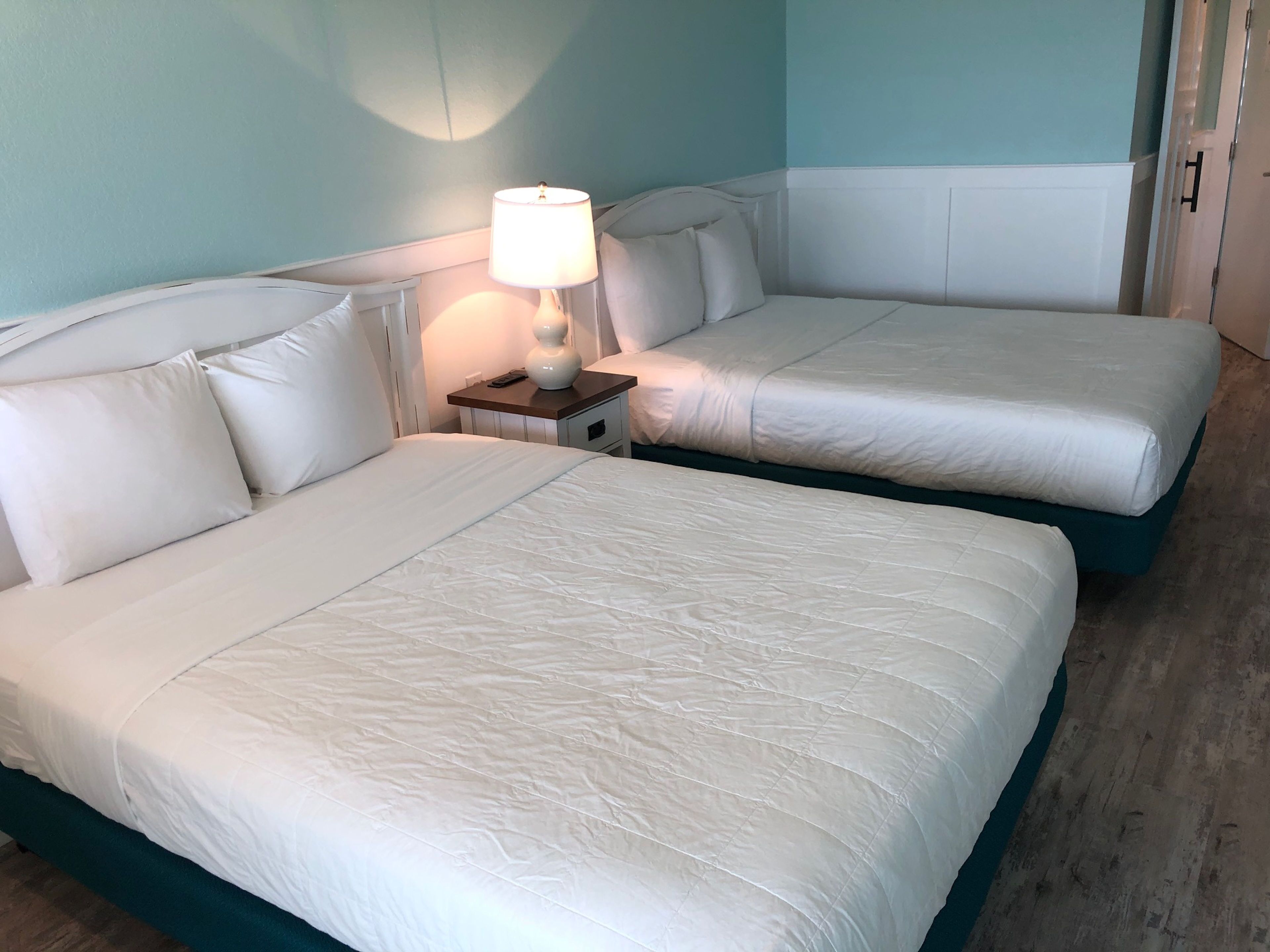 Une chambre avec deux lits, chacun étant équipé de draps blancs et d’une table de chevet avec une lampe.