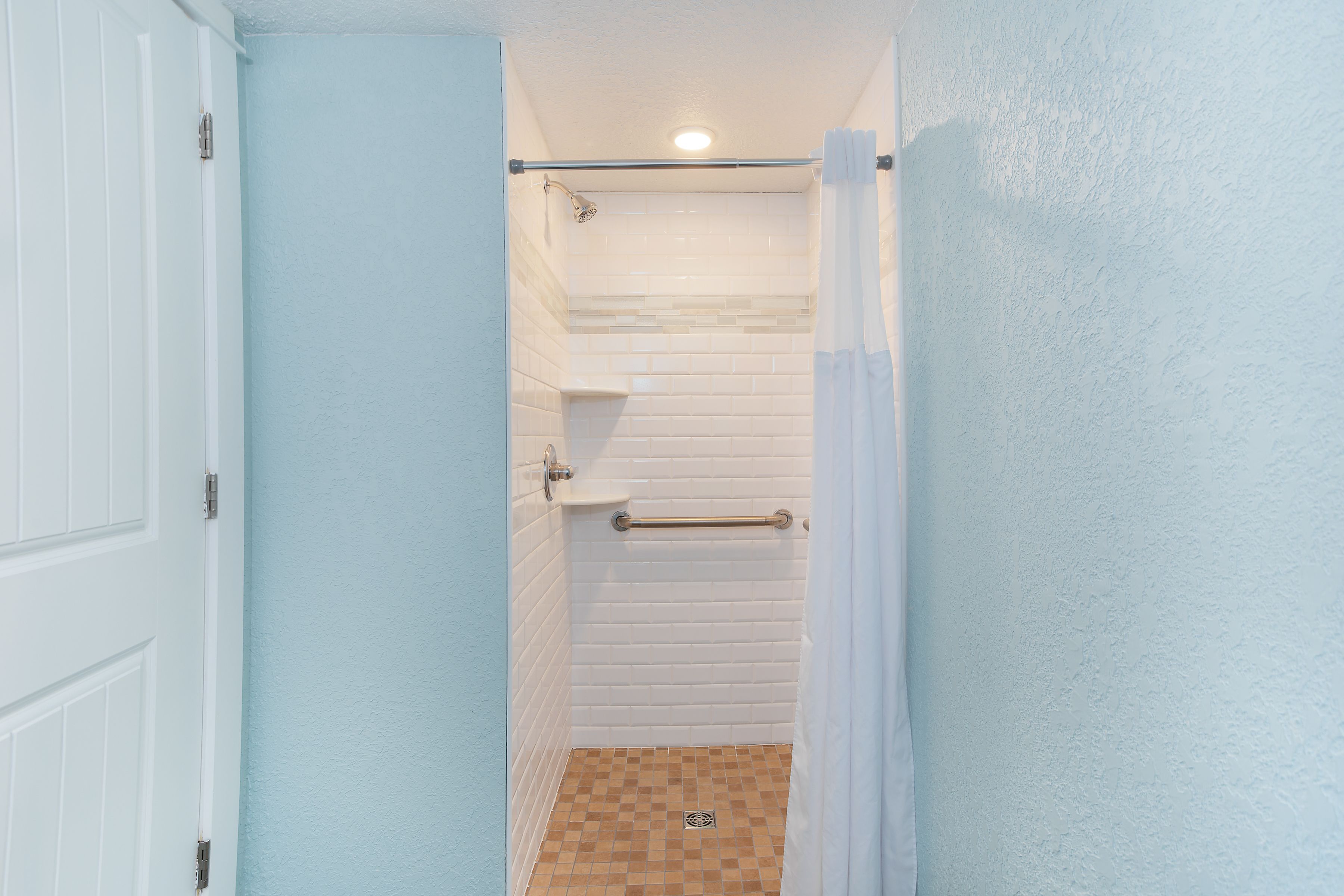 Um banheiro com paredes azulejadas em branco, um chuveiro com porta de vidro e uma porta branca.