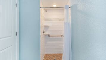 Um banheiro com paredes azulejadas em branco, um chuveiro com porta de vidro e uma porta branca.