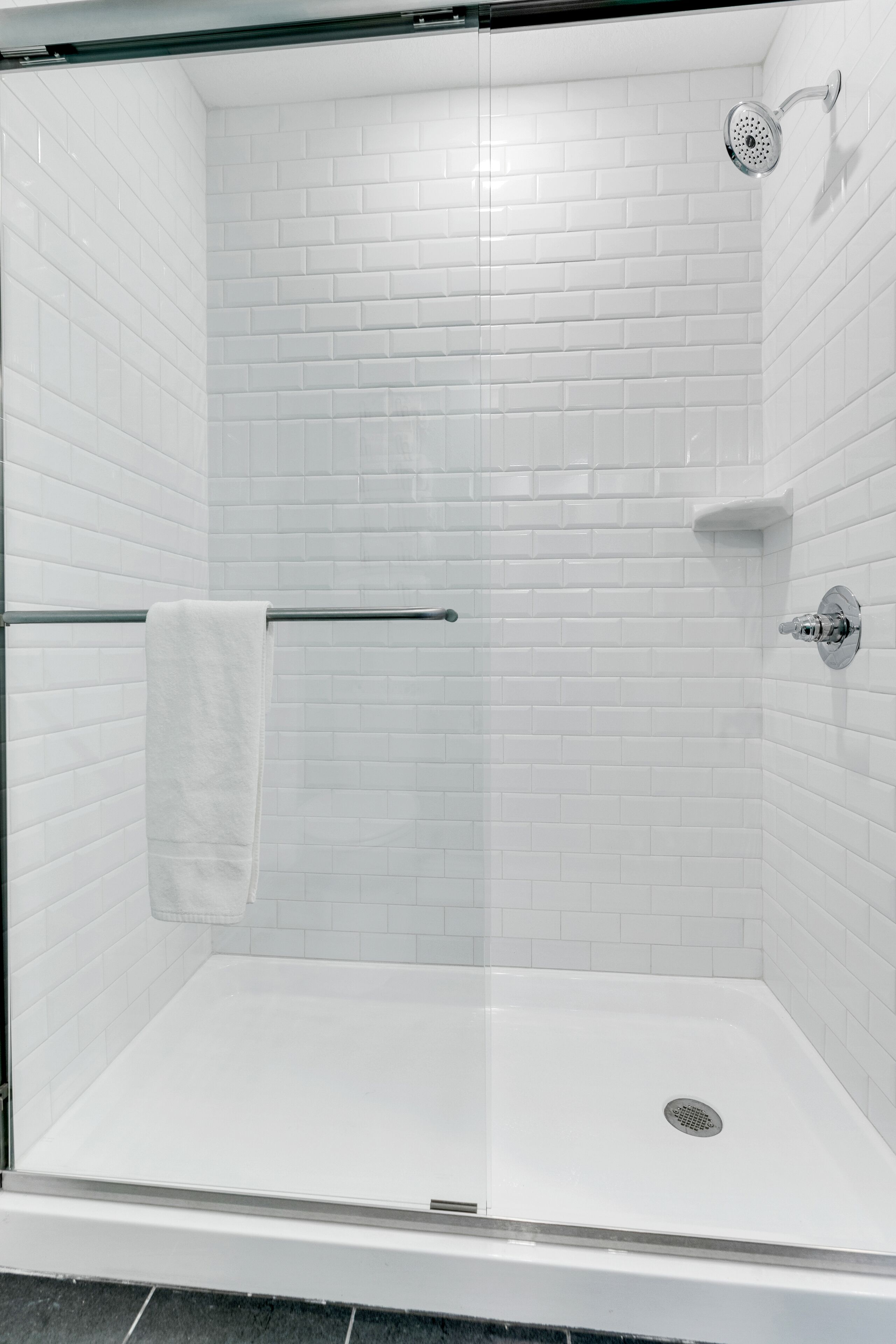A glass-enclosed shower with white tiled walls and a white floor.