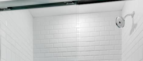 Ducha con cerramiento de vidrio, paredes de azulejos blancos y piso blanco.