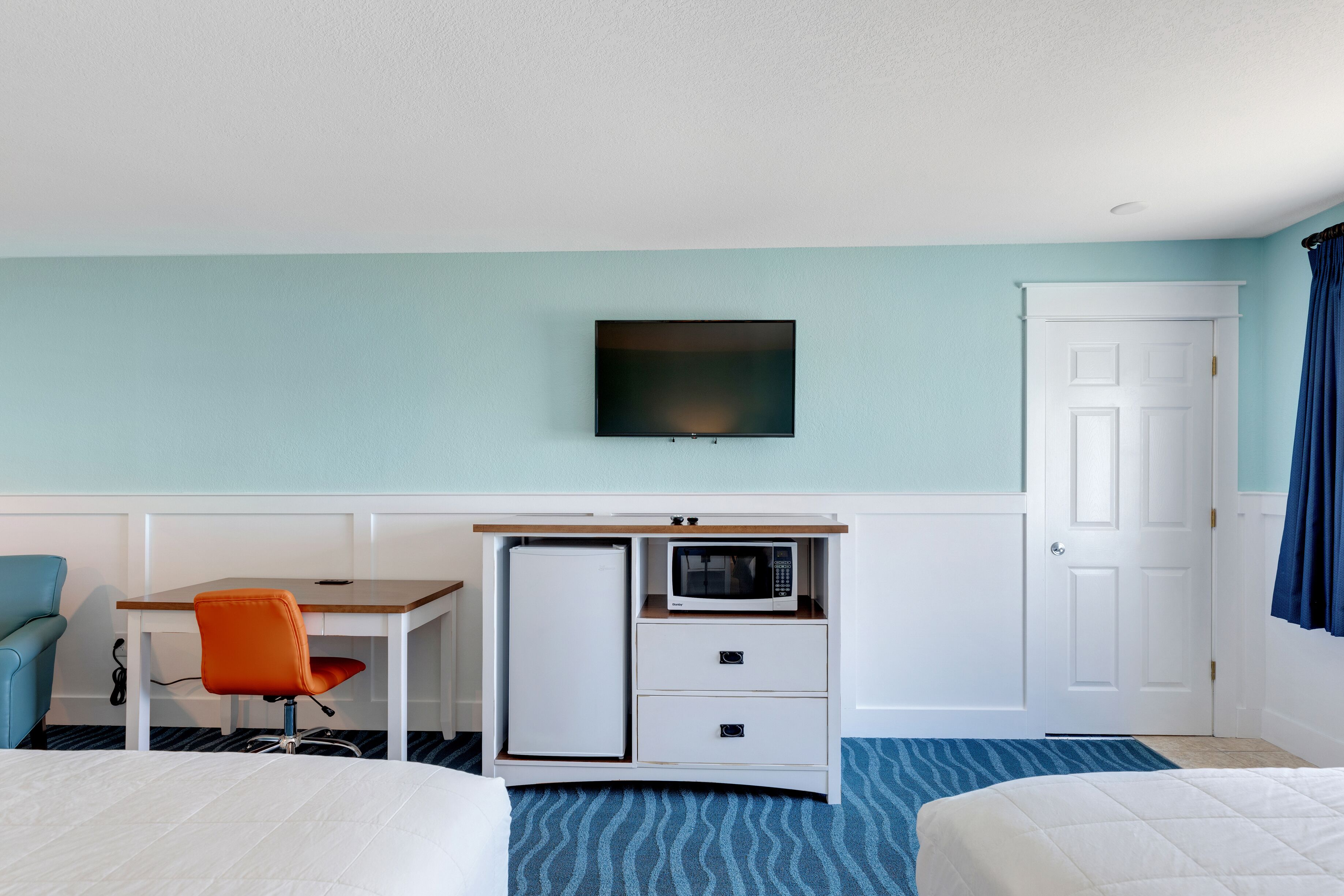 A hotel room with a bed, a desk with a microwave, a TV, and a door with curtains.