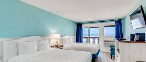 A hotel room with two beds, a desk, a chair, and a window with a view of the sea.