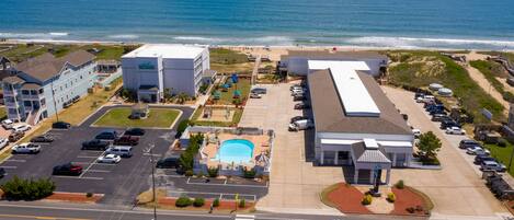 An aerial view of a coastal hotel with a swimming pool, parking lot, and ocean view.