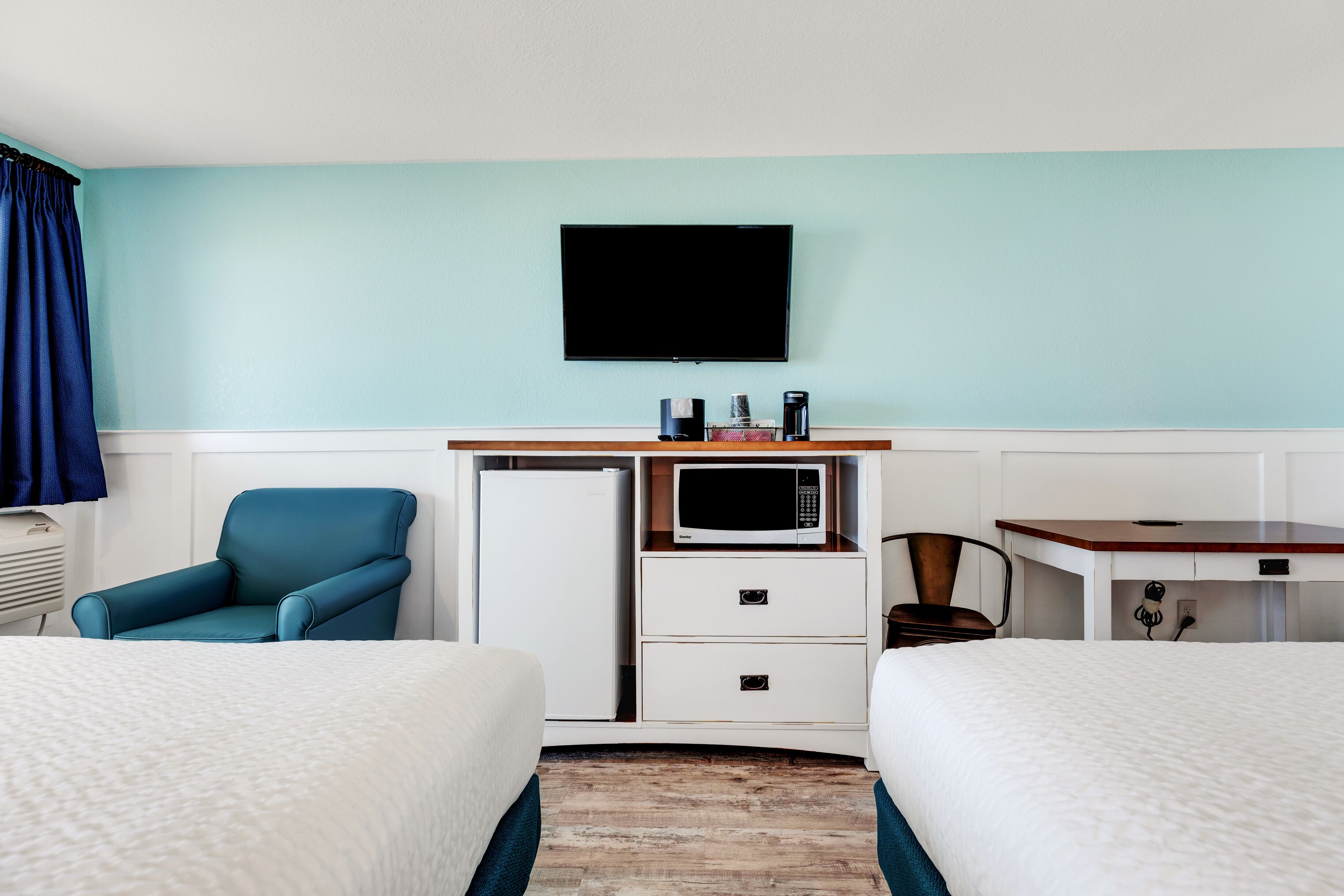 Habitación de hotel con dos camas, un escritorio con microondas, televisor y una silla.