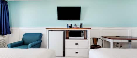A hotel room with two beds, a desk with a microwave, a TV, and a chair.