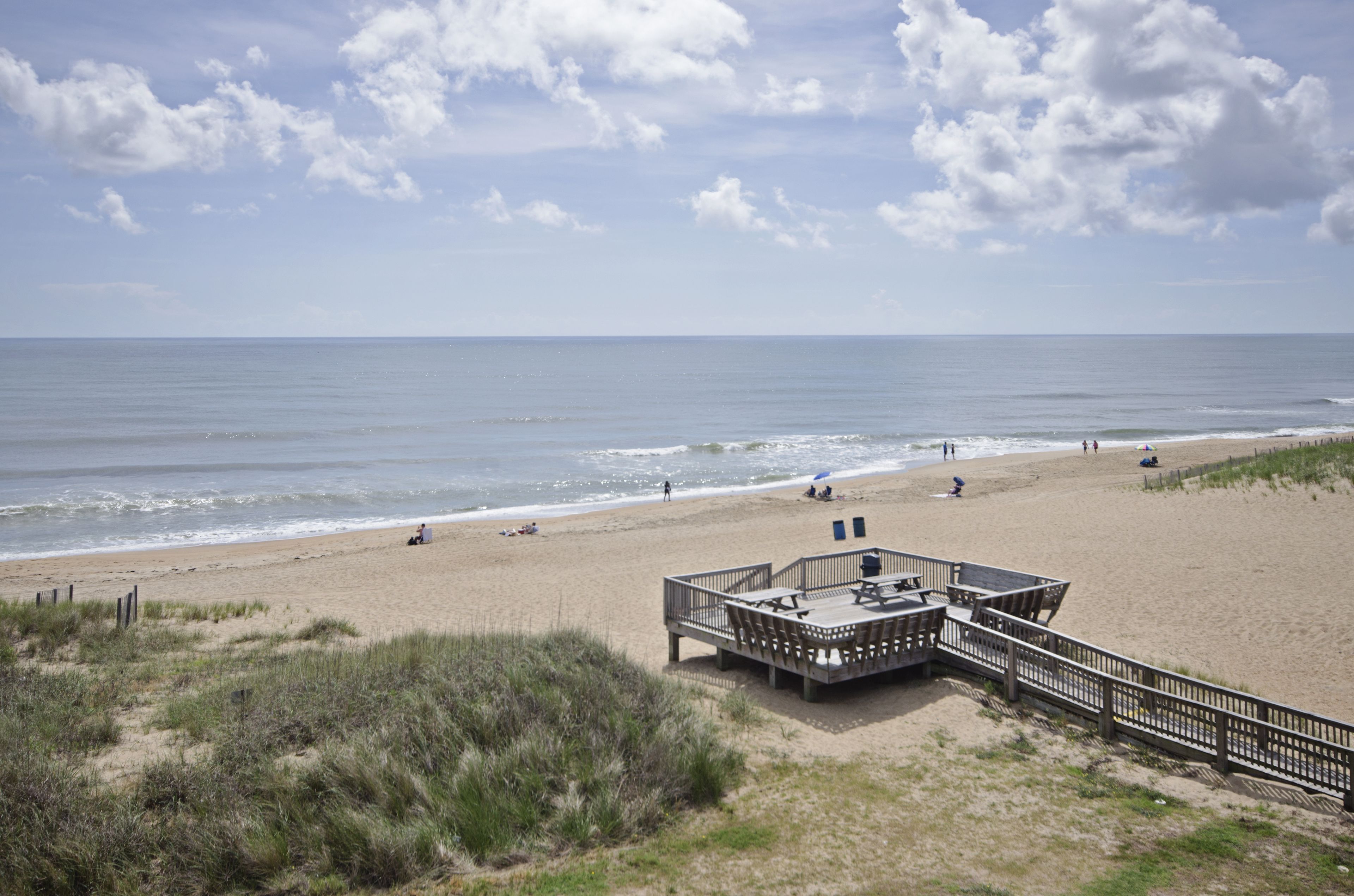 A beach with a wooden deck and lounge chairs overlooking the ocean.
