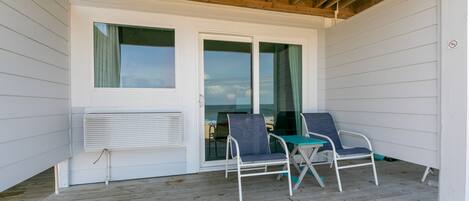 A covered porch with two chairs and a table, wooden ceiling beams, and a sliding glass door.