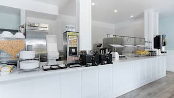 A clean, modern breakfast bar with a refrigerator, coffee machines, and a variety of food items.