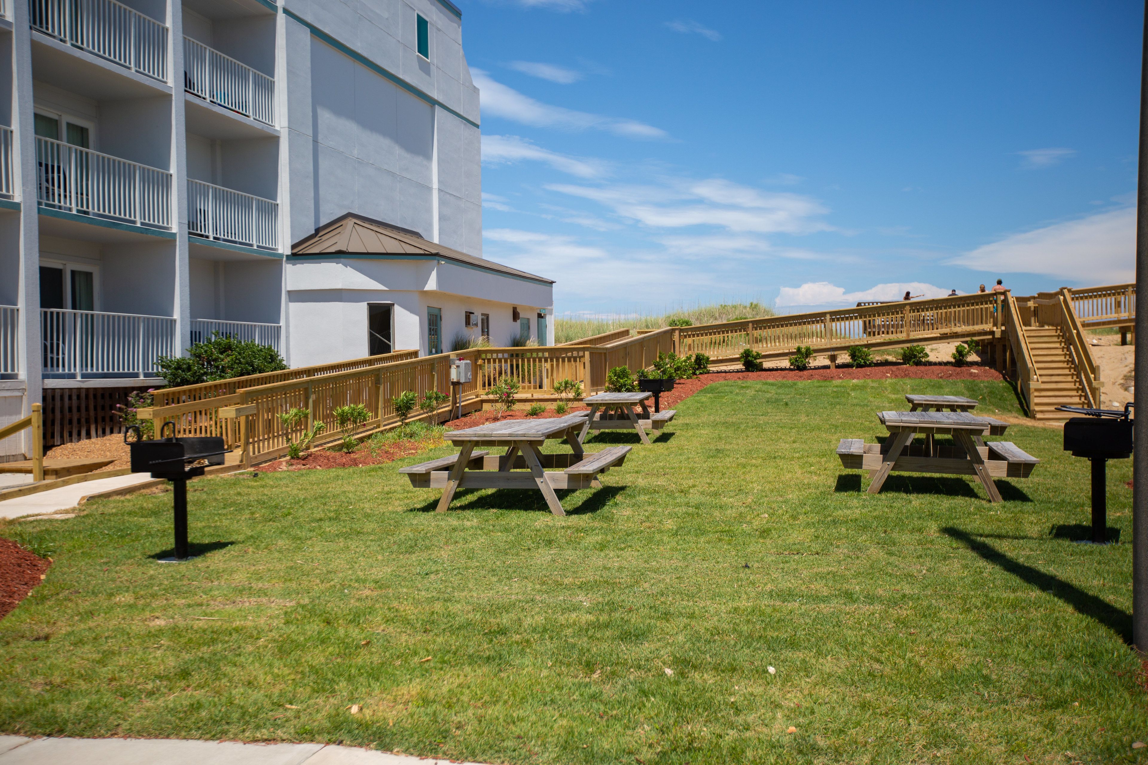 Een woongebouw met een witte gevel, meerdere balkons en een houten terras met picknicktafels.