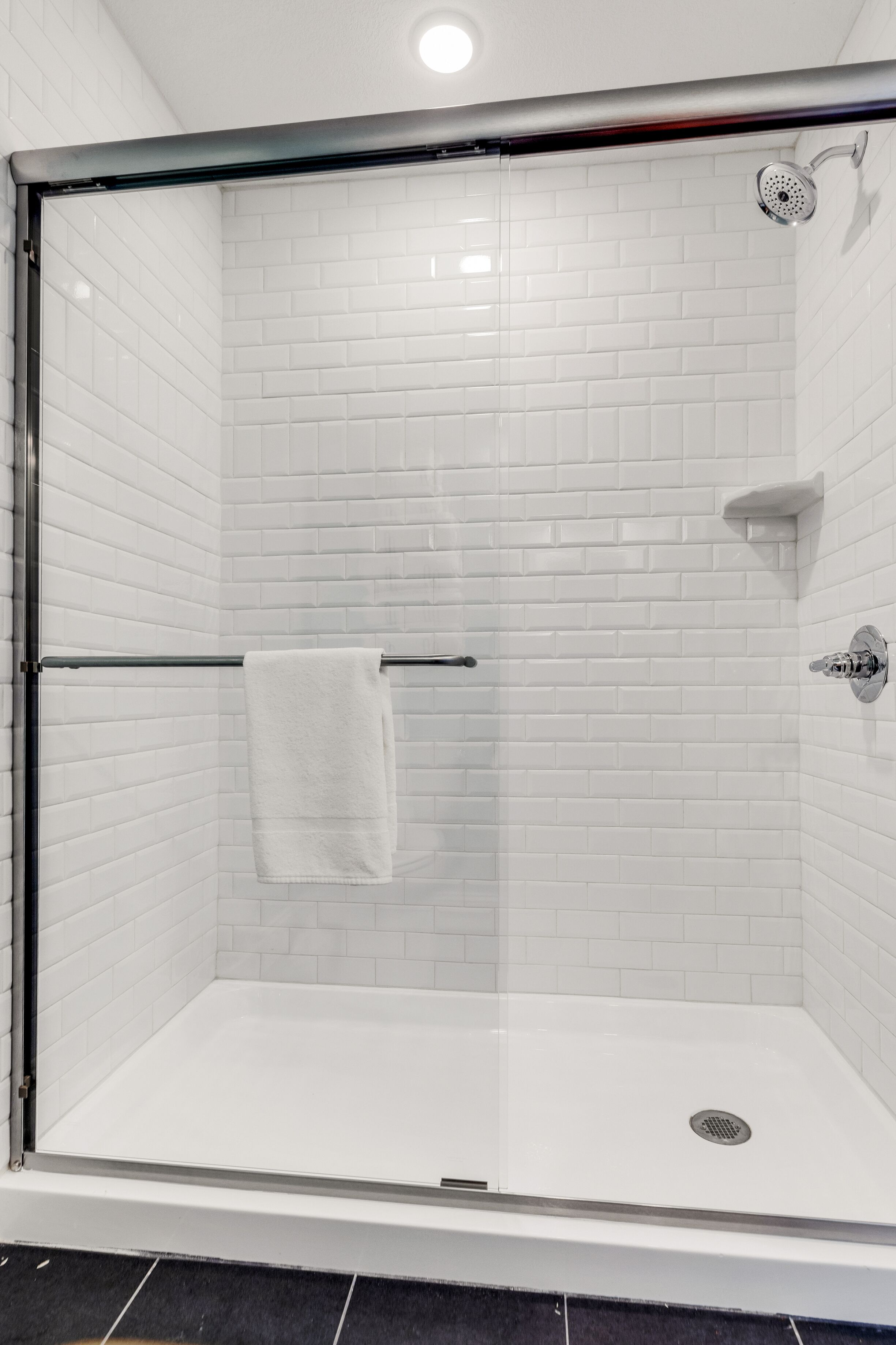 A glass-enclosed shower with white tiled walls and a visible drain.