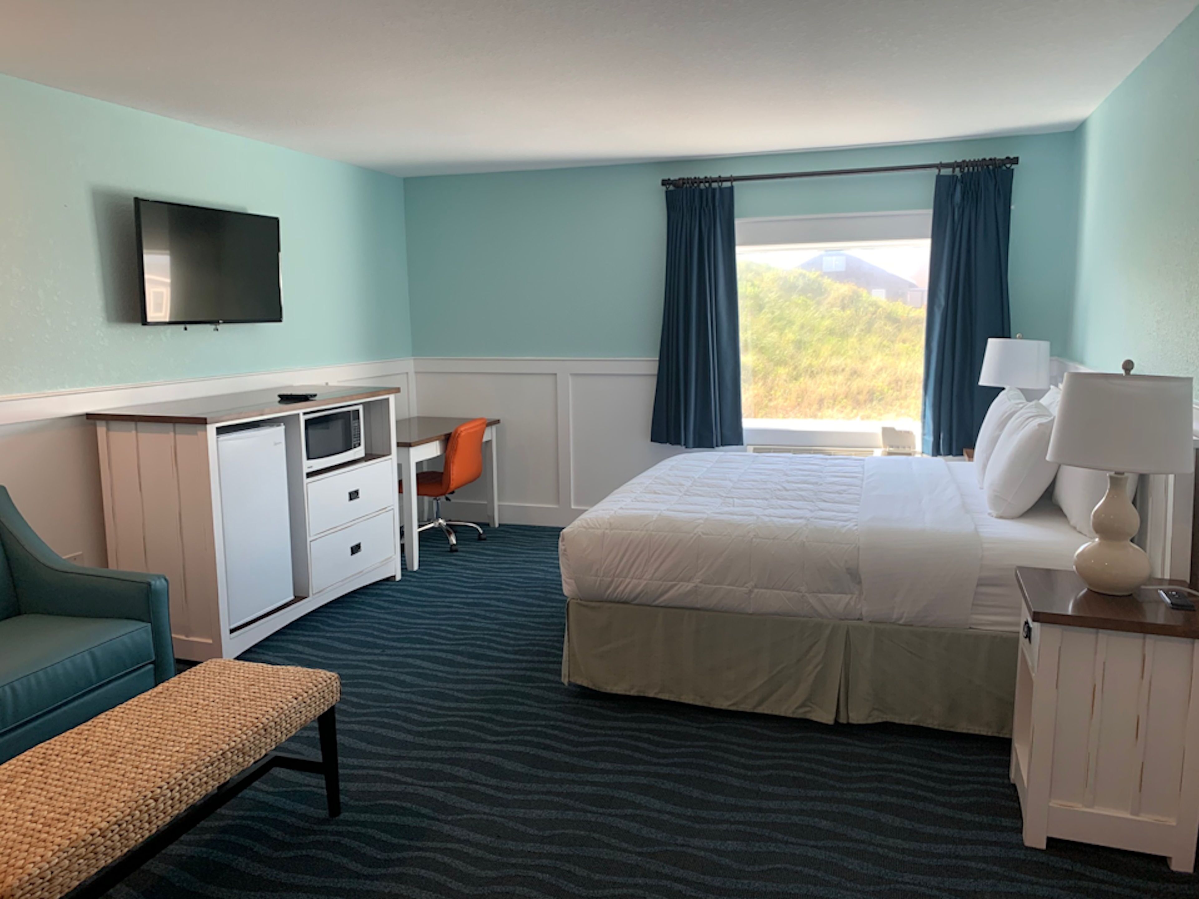 A hotel room with a bed, desk, chair, TV, and window with curtains.