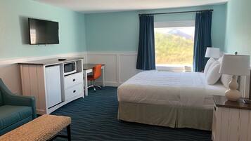 A hotel room with a bed, desk, chair, TV, and window with curtains.