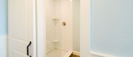 A bathroom with white subway tiles, a shower with a hexagonal floor pattern, and a white door with a black handle.