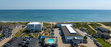 Vista aérea de un hotel frente al mar con piscina, aparcamiento y acceso a la playa.