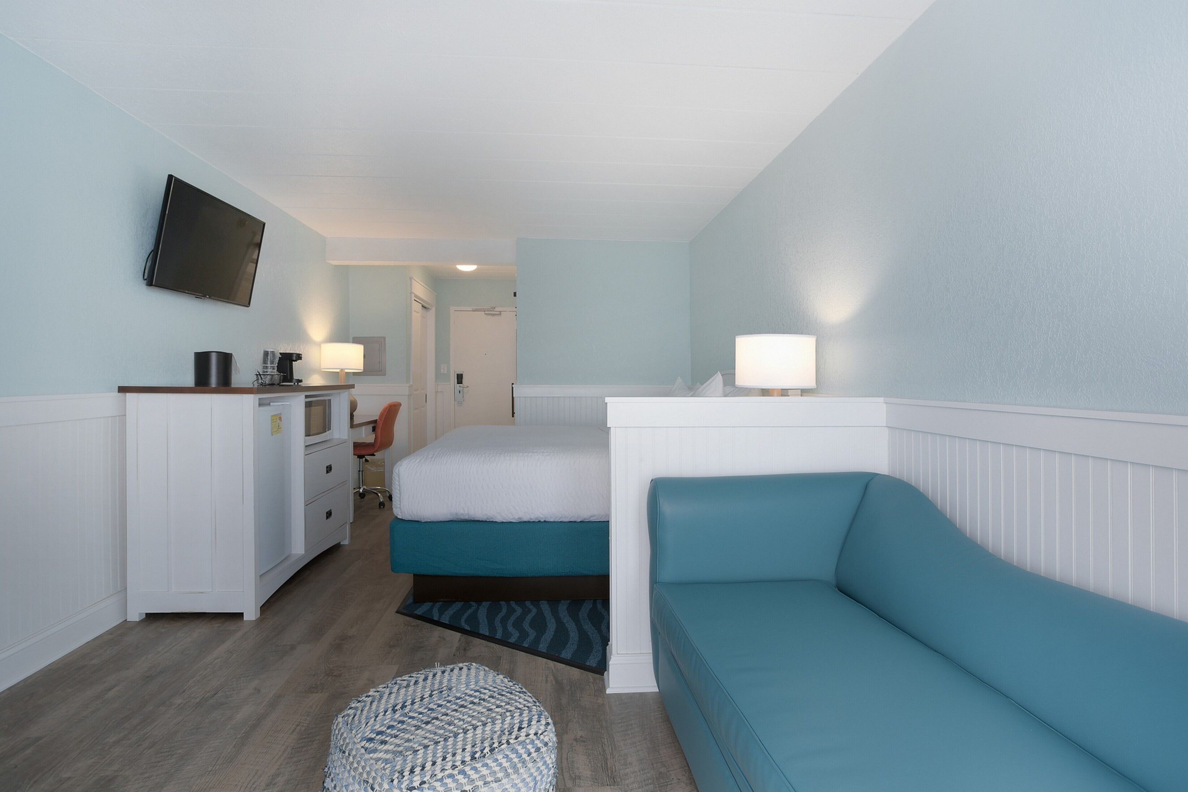 A room with a bed, a desk, a chair, a television, and a lamp.