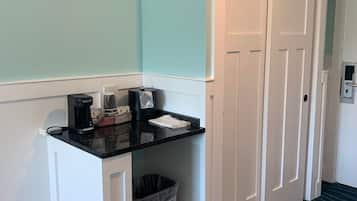 A small kitchenette with a coffee maker, trash can, and a white door.