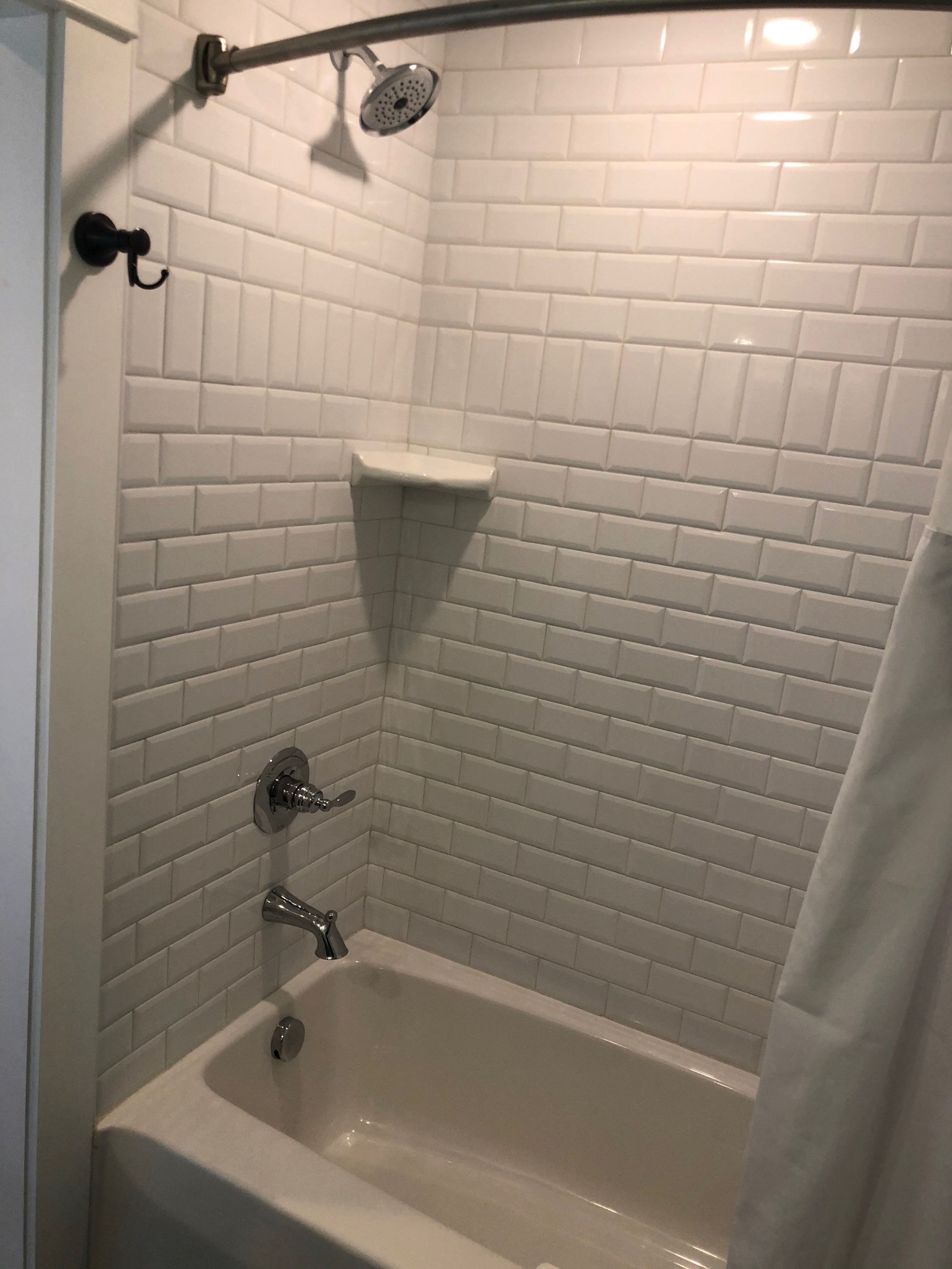 Ein Badezimmer mit weißen, in U-Form angeordneten Fliesen, einer Badewanne, einer Duschbrause und einem Handtuchhalter.